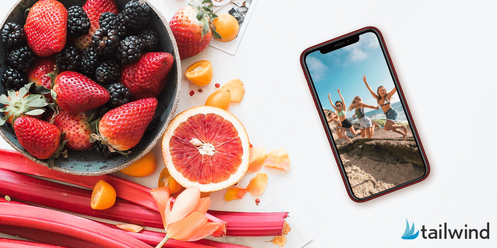 A bowl of mixed berries, sliced grapefruit, and rhubarb sits on a white surface next to a smartphone displaying three people jumping on the beach; Tailwind logo in the corner hints at instagram pods inspiration.