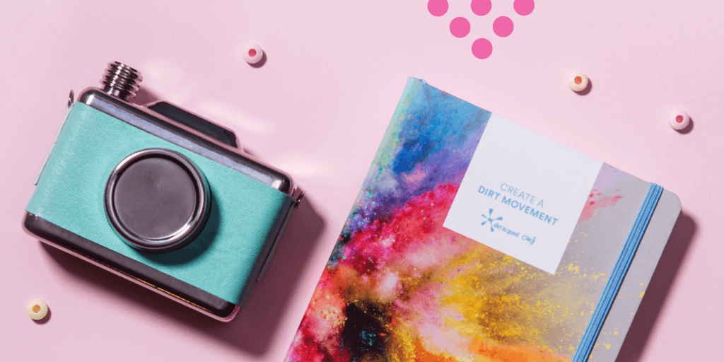A teal vintage camera and a colorful notebook with "Create a Dirt Movement" on the cover sit on a pink surface, surrounded by small round beads—perfect props for your next how to schedule instagram stories video.