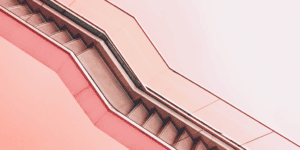 An abstract, angled photo of a staircase with zigzag lines and smooth pink and coral walls evokes a modern, geometric vibe—much like wondering, "why did my Pinterest monthly viewers decrease?" in the ever-changing world of design trends.