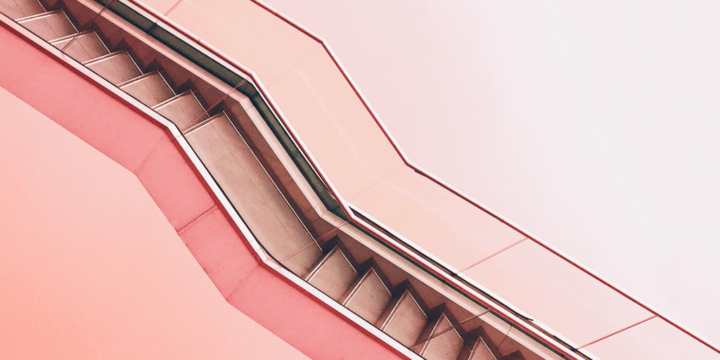 An abstract, angled photo of a staircase with zigzag lines and smooth pink and coral walls evokes a modern, geometric vibe—much like wondering, "why did my Pinterest monthly viewers decrease?" in the ever-changing world of design trends.